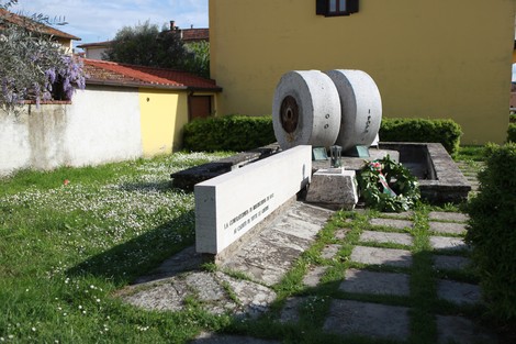 Monumento ai caduti di Soci con struttura in pietra, decorato da fiori e circondato da un giardino curato.