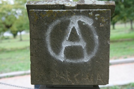 Cippo a Meuret con simbolo anarchico, situato in un contesto naturale.