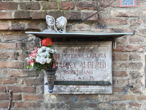 Lapide commemorativa a Caudana con fiori e una statuetta, dedicata a un martire partigiano.