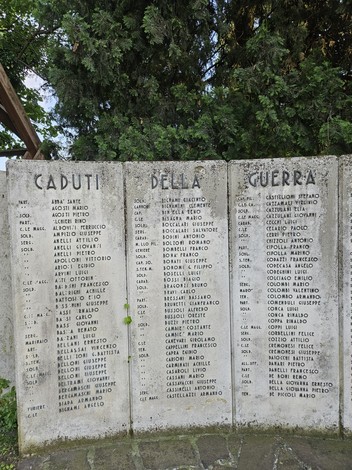 Monumento ai Caduti con nomi incisi in memoria dei soldati, circondato da alberi e vegetazione.