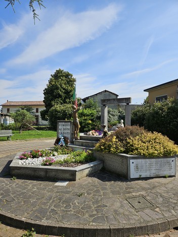 Monumento commemorativo con statue, fiori e bandiera, dedicato a Beretta, Carletti e Castagna in un parco.