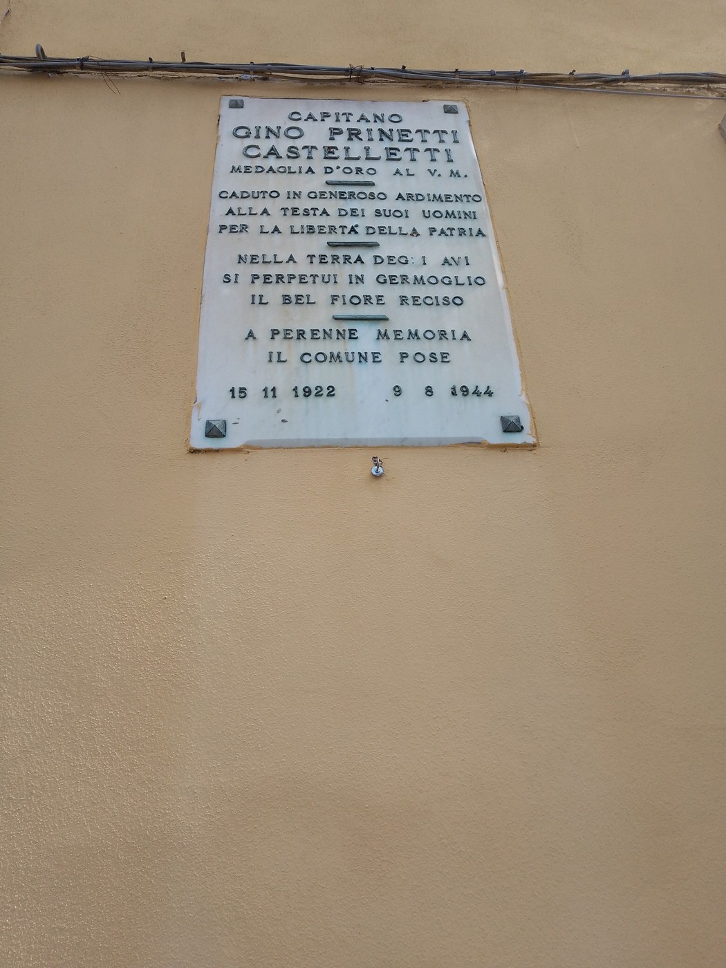 Lapide commemorativa dedicata a Gino Prinetti Castelletti, con riferimento alla sua medaglia d'oro e al sacrificio per la patria.