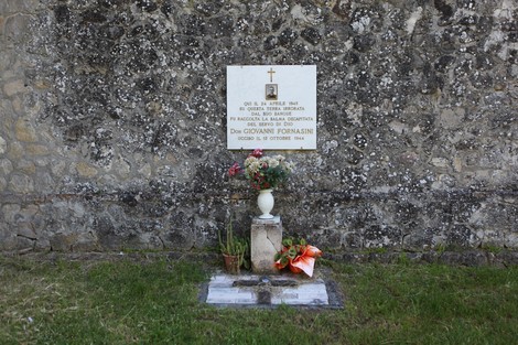 Lapide commemorativa di Giovanni Fornasini, situata in un contesto semplice e rispettoso. Decorata con fiori.