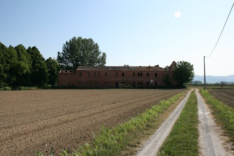 Lapide della Tabaccaia di Prato Grande, con vista su un edificio fatiscente e campi circostanti.