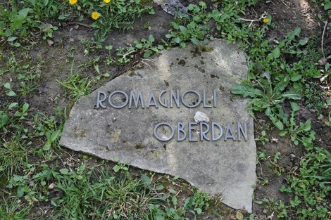 Monumento del cimitero di Stia, con iscrizioni su una pietra, immerso nel verde e nella natura circostante.