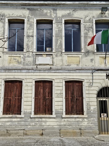 Facciata di un edificio con finestre chiuse da persiane in legno, bandiera italiana e pareti invecchiate.