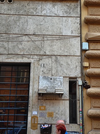 Lapide in muratura dedicata a un astrologo, affissa su una parete in un contesto urbano.