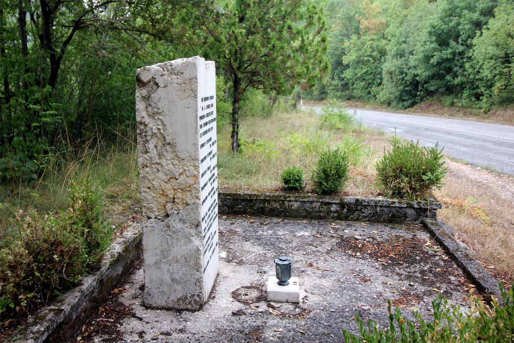 Cippo commemorativo dedicato ai partigiani uccisi a Colle di Postignano, immerso nella natura.