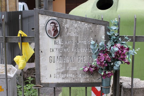 Lapide commemorativa dedicata a Guadagni Pietro, con fiori e decorazioni, in un contesto urbano.