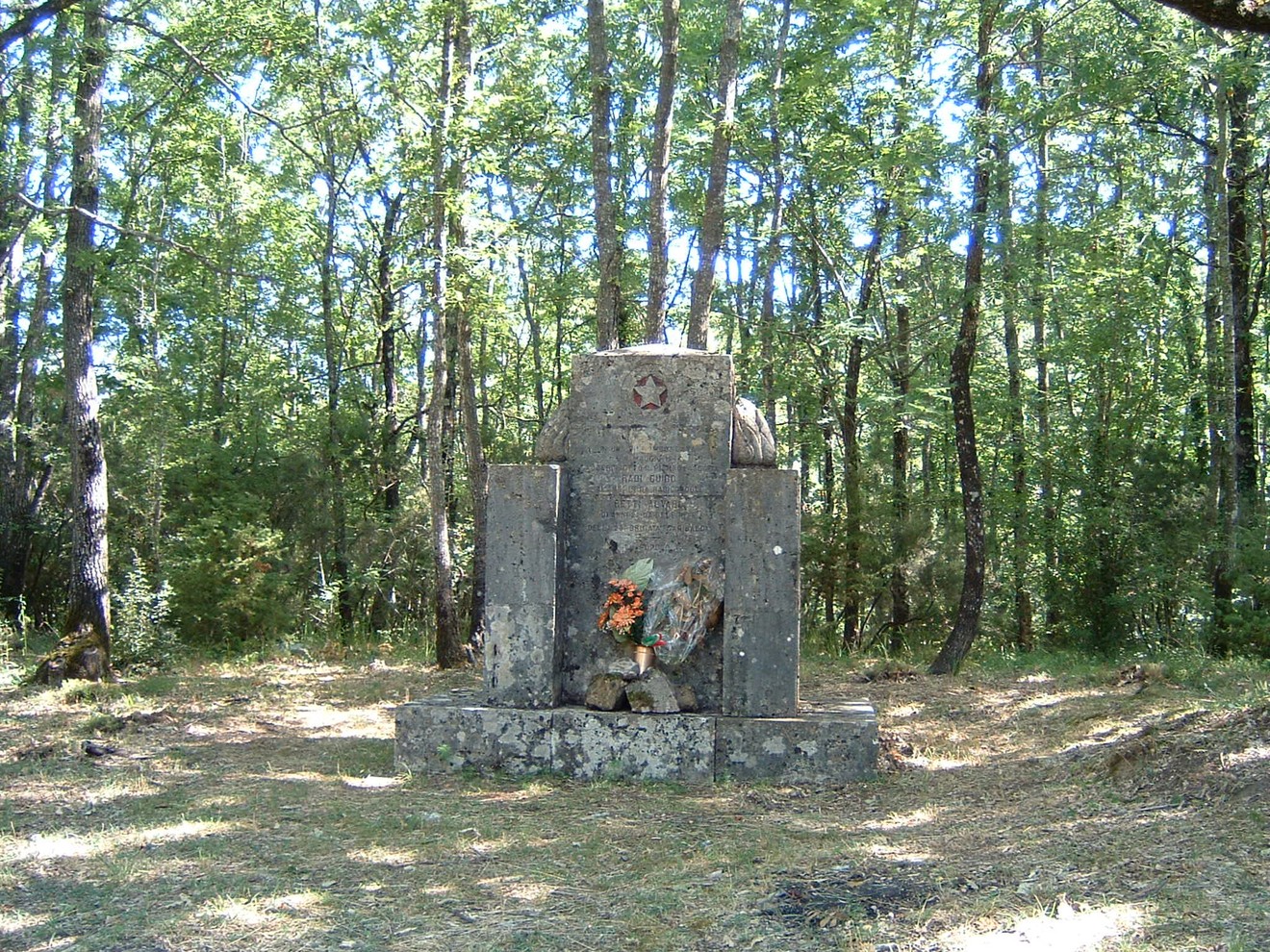 Monumento a Radi e Betti immerso nella natura, circondato da alberi e un terreno erboso.