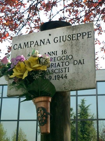 Targa commemorativa in onore di Giuseppe Campana, con fiori artificiali, affissa su un palo.
