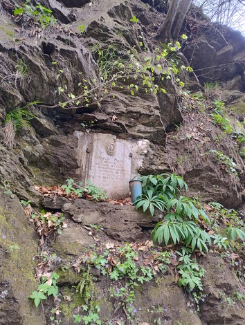 Lapide incastonata tra le rocce di una parete, circondata da vegetazione e segni del tempo.