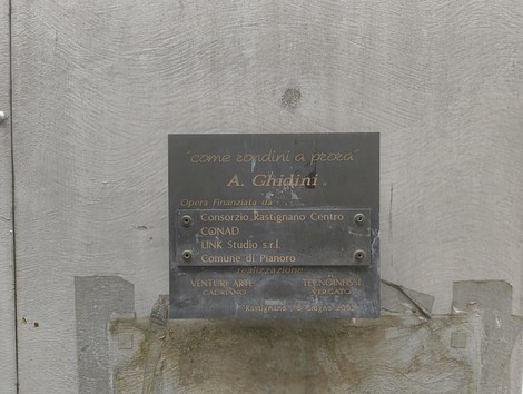 Monumento a Piccinini con targa commemorativa su sfondo grigio e dettagli di design.