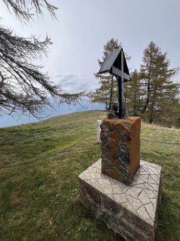 Monumento a Ghiotti su un pedestallo in un paesaggio naturale, circondato da alberi e cielo nuvoloso.
