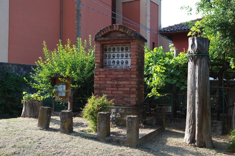 Cippo commemorativo dedicato ai caduti della Battaglia di Rasiglio, circondato da vegetazione e tronchi di legno.