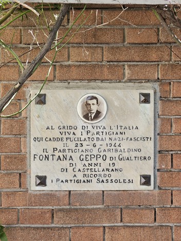 Lapide commemorativa dedicata a Fontana Geppo, partigiano caduto, con decorazioni floreali sullo sfondo.