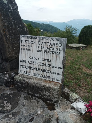 Monumento ai caduti con lapide commemorativa in un paesaggio montano. Ricordo di giovani partigiani.
