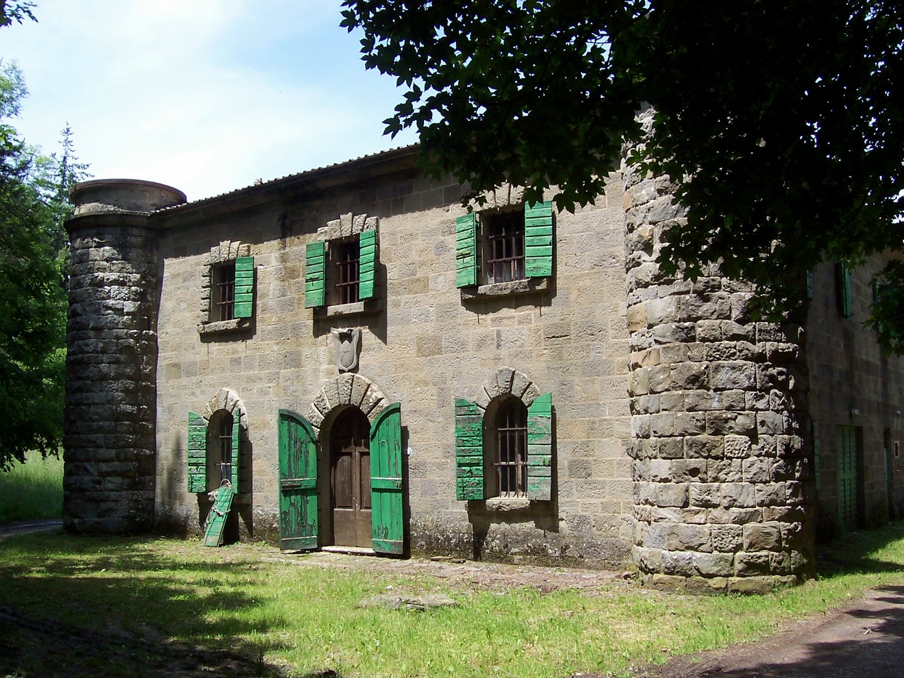 Lapide della Villa di Podernuovo, edificio storico con finestre verdi immerso nella natura.