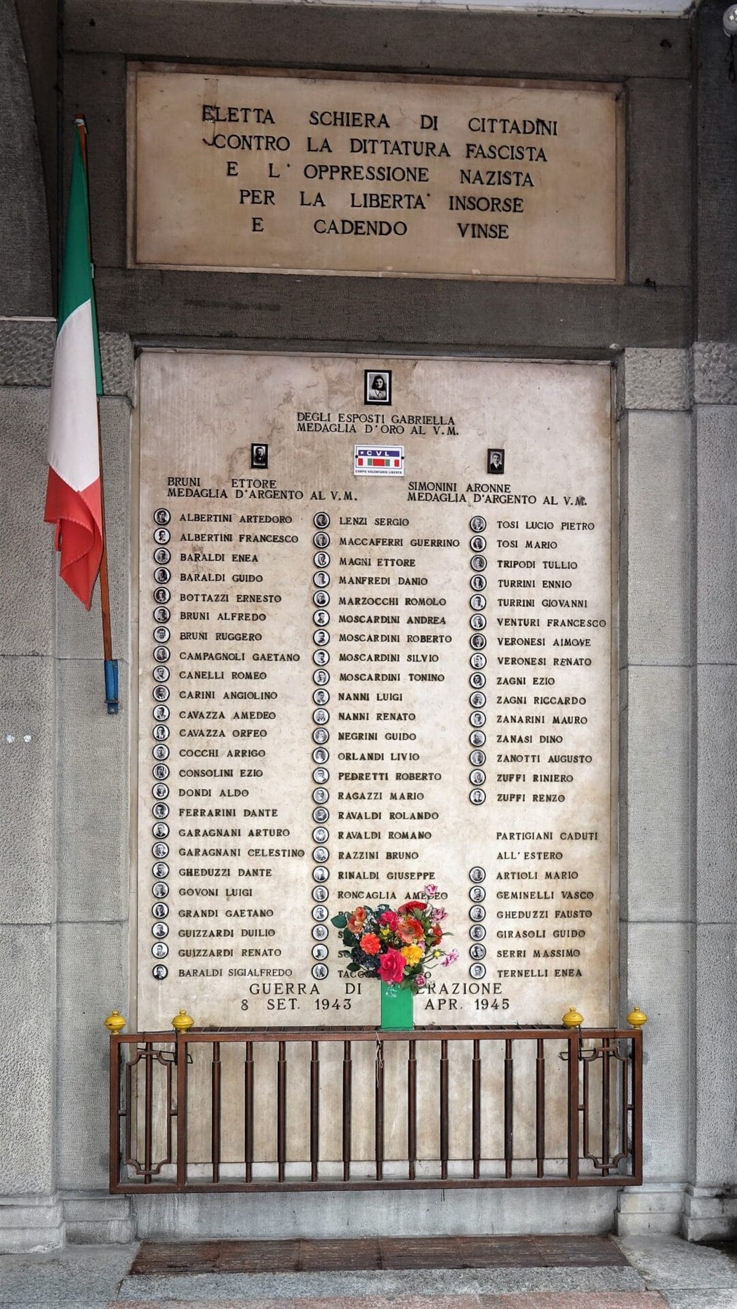 Monumento commemorativo ai caduti partigiani, con nomi incisi e decorazioni floreali in omaggio.