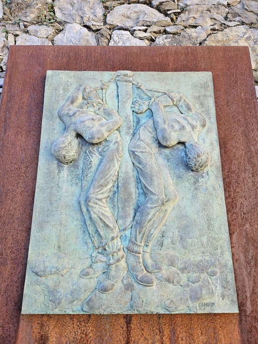 Scultura che rappresenta due figure umane in un atto di unione e tensione, collocata in un contesto di pietra.
