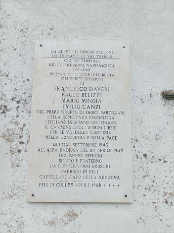 Lapide commemorativa ai primi partigiani di Peli, situata in un contesto storico significativo.