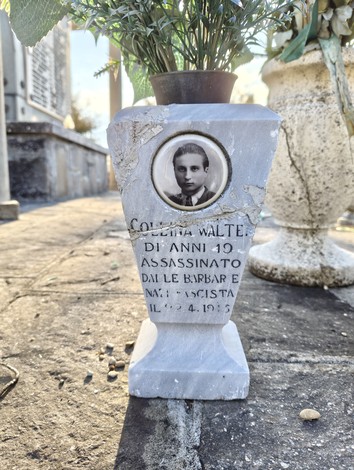Sacrario ai caduti con una lapide commemorativa di un giovane assassinato, decorata con fiori.
