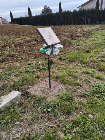 Lastra a Luschi su un supporto verticale, circondata da un campo arato e decorata con un nastro tricolore.
