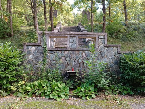 Il Memoriale dei caduti della Benedicta, immerso nella natura, con gradini in pietra e verdeggianti piante circostanti.