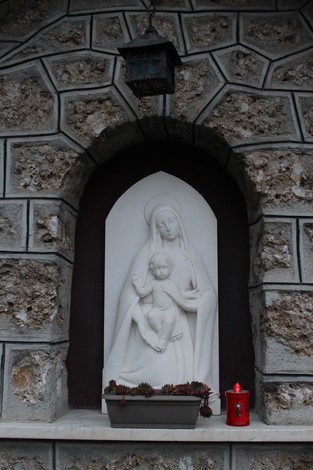 Tabernacolo della 51a Sezione Sanità con statua di Madonna e bambino su sfondo in pietra. Decorato con lanterna e fiori.