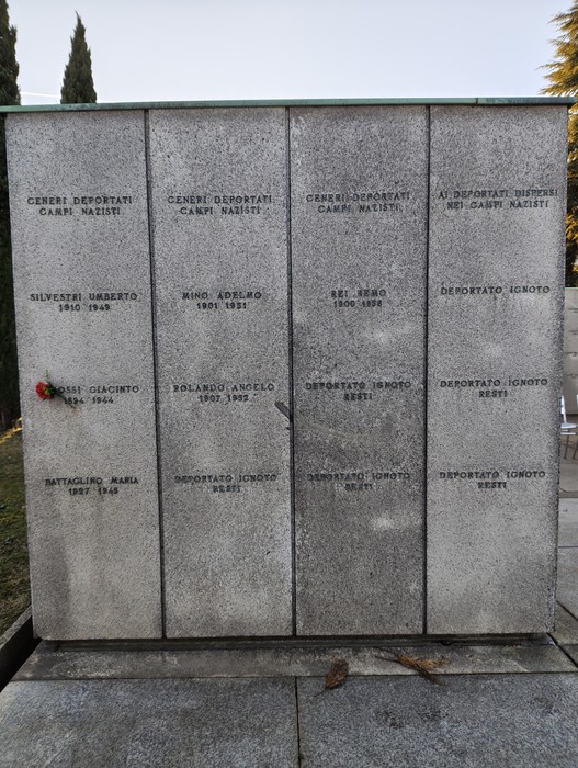 Monumento commemorativo nel Campo della Gloria con nomi di deportati e un omaggio floreale.