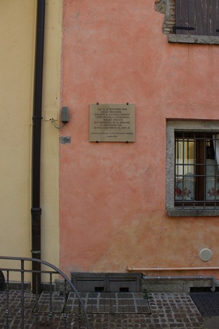 Lapide commemorativa su un muro di colore rosa, con dettagli architettonici in primo piano.