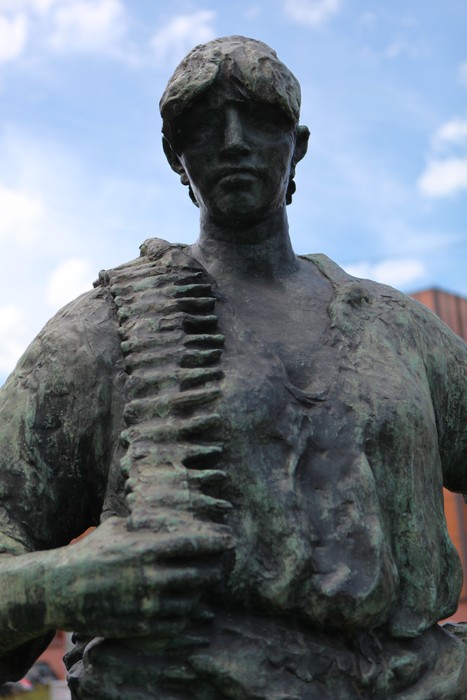 Scultura di un partigiano, rappresentante la lotta per la libertà, con espressione determinata e bandoliera sulla spalla.