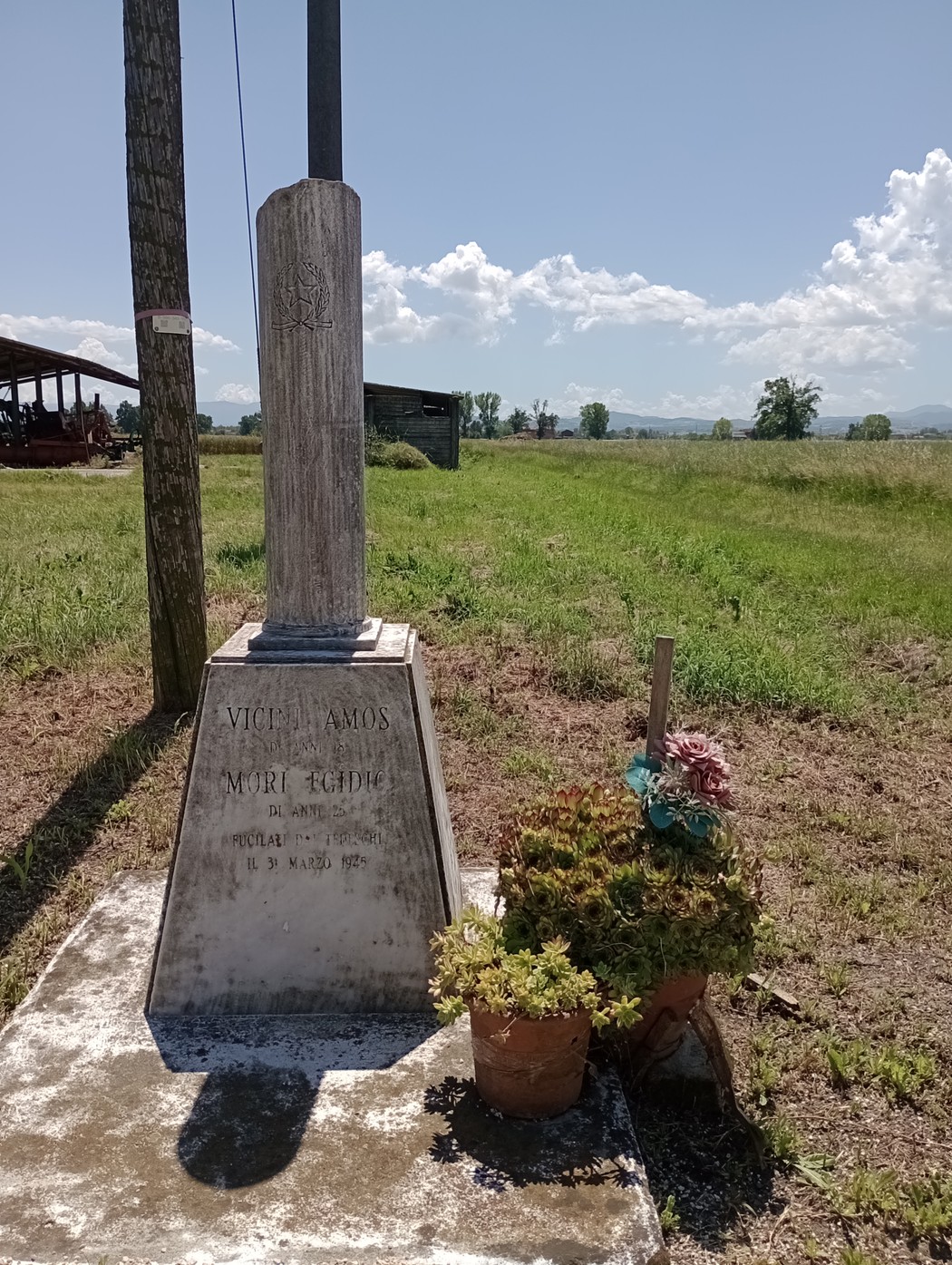 Cippo commemorativo dedicato a Vicini e Mori, situato in un'area rurale con vegetazione e cielo sereno.