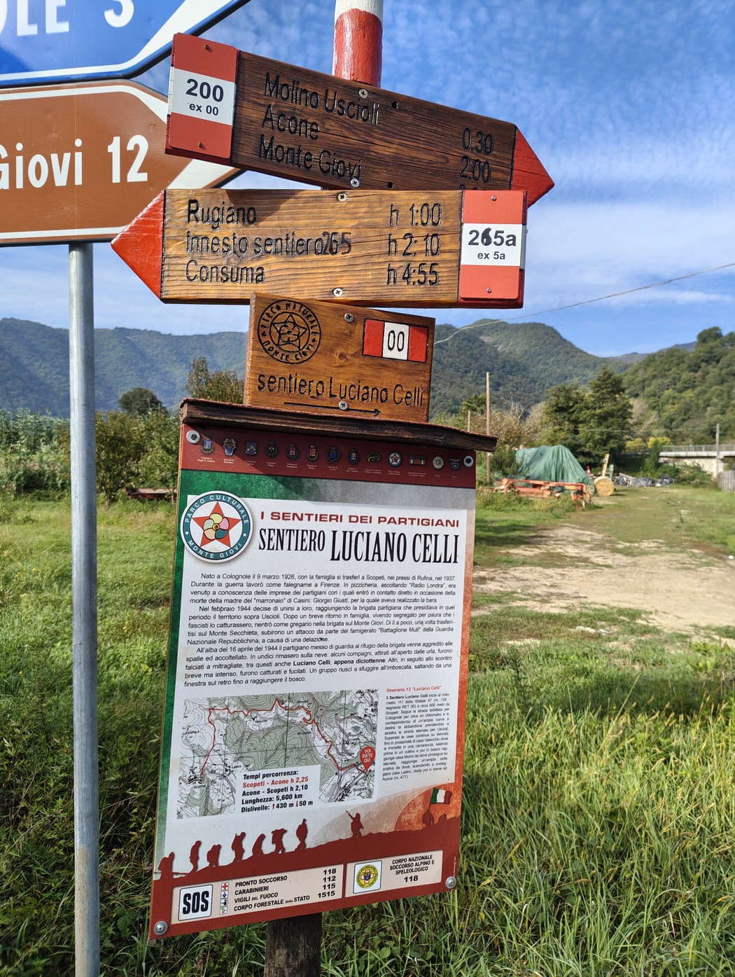 Cartelli segnavia in legno e pannello informativo con mappa del sentiero, lungo una strada di montagna.