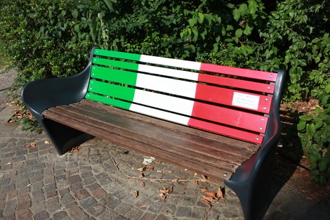 Panchina decorata nei colori della bandiera italiana, immersa nel verde della vegetazione circostante.