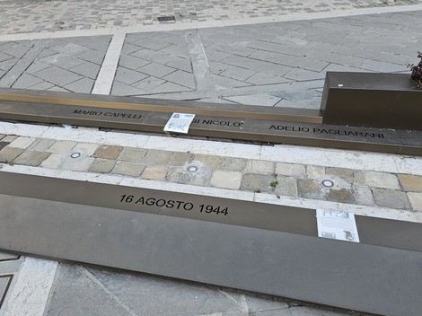 Monumento ai Tre Martiri con lastre commemorative e date storiche incise, situato in un contesto urbano.