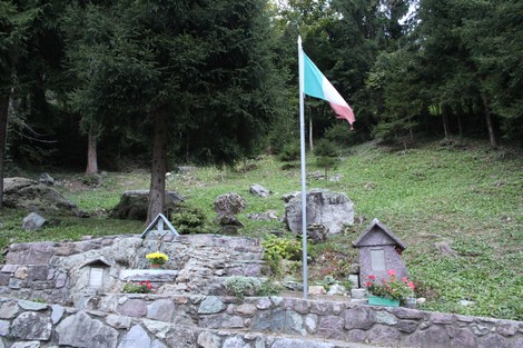 Monumento commemorativo con bandiera italiana e paesaggio naturale circostante.