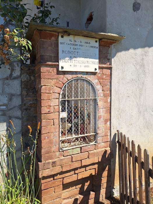 Lapide commemorativa in mattoni con grata, dedicata a Robotti e Perotti, situata in un ambiente rurale.