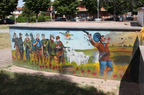 Murale colorato che raffigura figure storiche e scene di lotta, sullo sfondo di un paesaggio rurale.