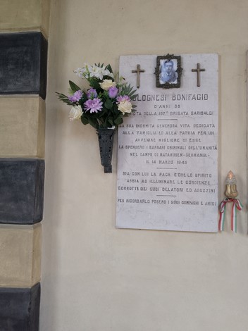 Lapide commemorativa a Colognesi con fiori e foto, in memoria di Bonifacio. Riflessione sulla vita e l'eredità.