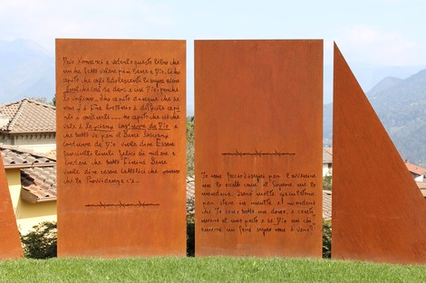 Monumento a Seghezzi con pannelli metallici e paesaggio montano sullo sfondo, riflettendo arte e memoria.