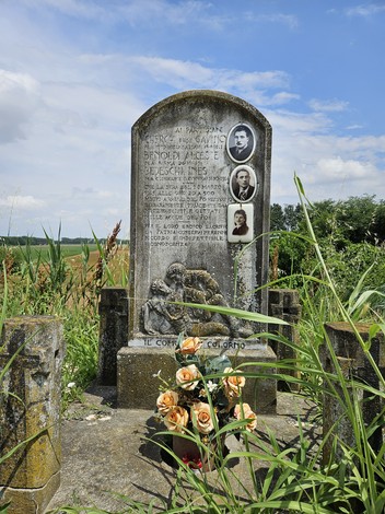 Cippo commemorativo in un'area rurale, circondato da vegetazione e fiori, dedicato a Cherchi, Benoldi e Bedeschi.