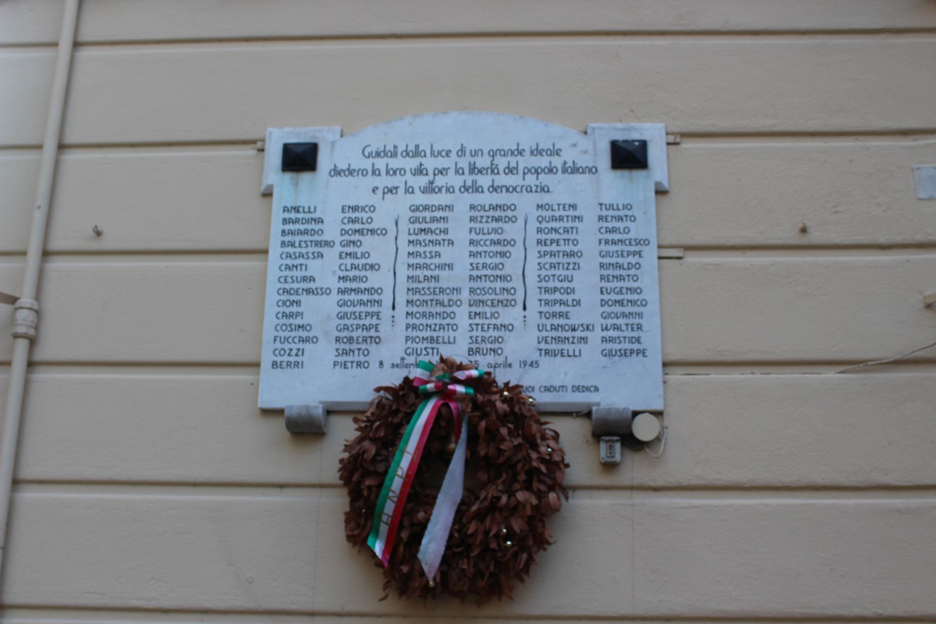 Lapide commemorativa dedicata ai caduti per la libertà, con nomi incisi e corona di fiori decorata.