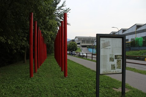 Memoriale del 29 gennaio 1945 con colonne rosse in un parco, circondato da vegetazione e un pannello informativo.