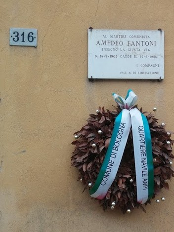 Lapide commemorativa dedicata ad Amedeo Fantoni, martire comunista, con una corona di foglie e nastri.