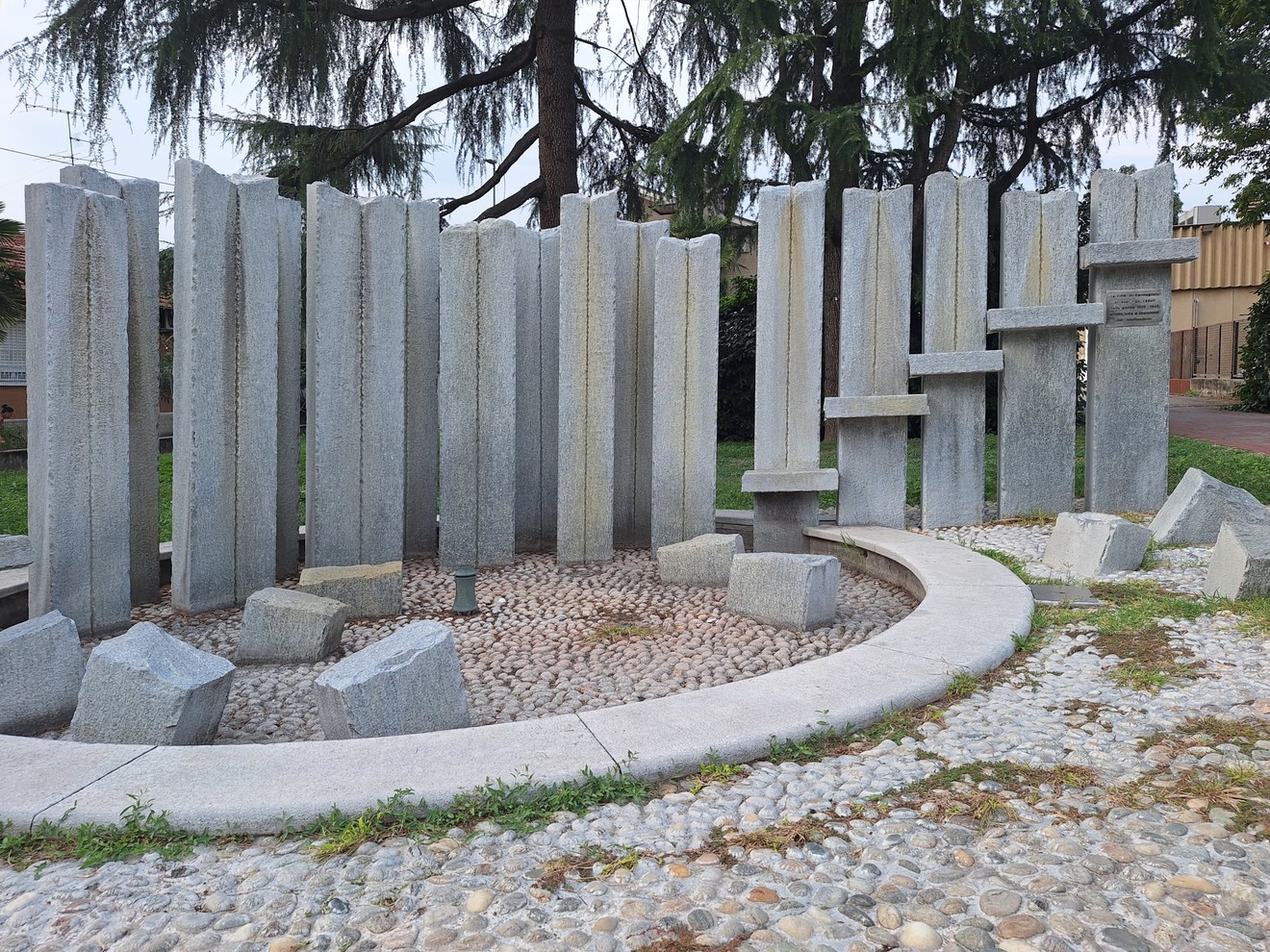 Monumento con pilastri di pietra disposti in semicerchio, alcuni con iscrizioni, in un'area pavimentata a ciottoli.
