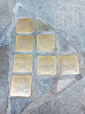 Sette pietre d'inciampo in ottone incastonate nel marciapiede, ciascuna con iscrizione incisa.