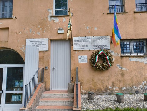 Lapidi commemorative di Pietraporciana, affiancate da una corona di fiori e bandiere, su una facciata storica.