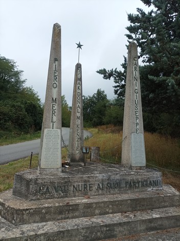 Monumento ai partigiani della Valnure, con obelischi e catene, immerso nella natura circostante.