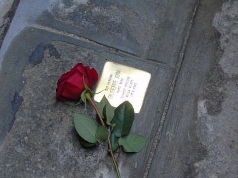 Pietra d'inciampo a Jona con una rosa rossa posata accanto su pavimento in pietra.